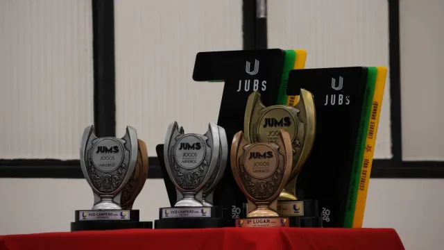 Troféus conquistados no JUMs e JUBs em cima de uma mesa com toalha vermelha