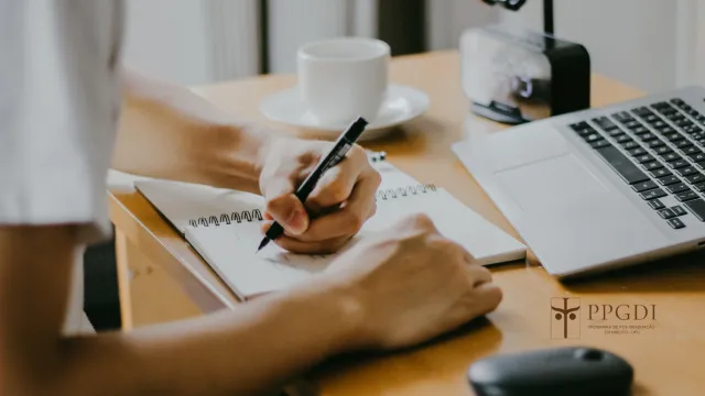 Estudante escrevendo em um caderno em frente ao computador