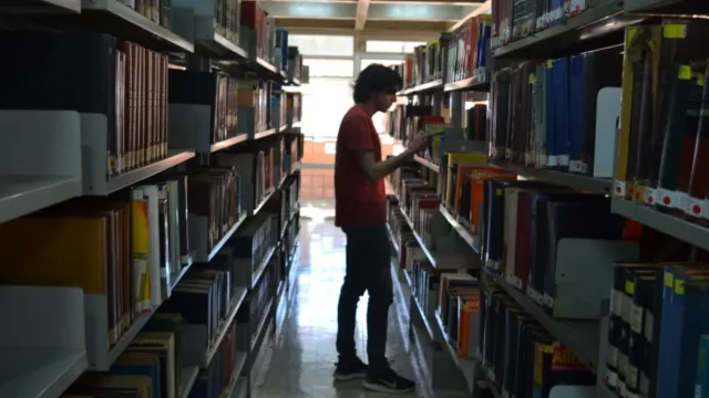 Homem vê livros em corredor da biblioteca da UFU
