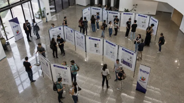 Pessoas no Hall de um prédio observam posteres de pesquisa