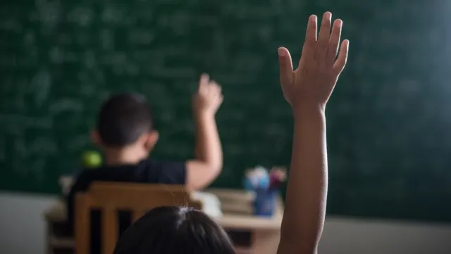crianças na sala de aula levantando a mão direita