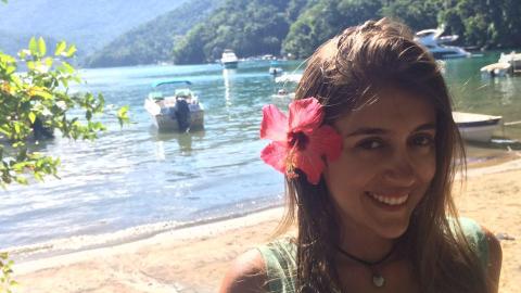 Foto da servidora Larissa de Lima, sorridente, com uma flor em uma das orelhas