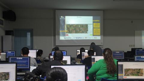 Na imagem, pessoas sentadas em frente telas de computadores