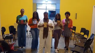 Na imagem, pessoas em pé segurando livro de autores negros.