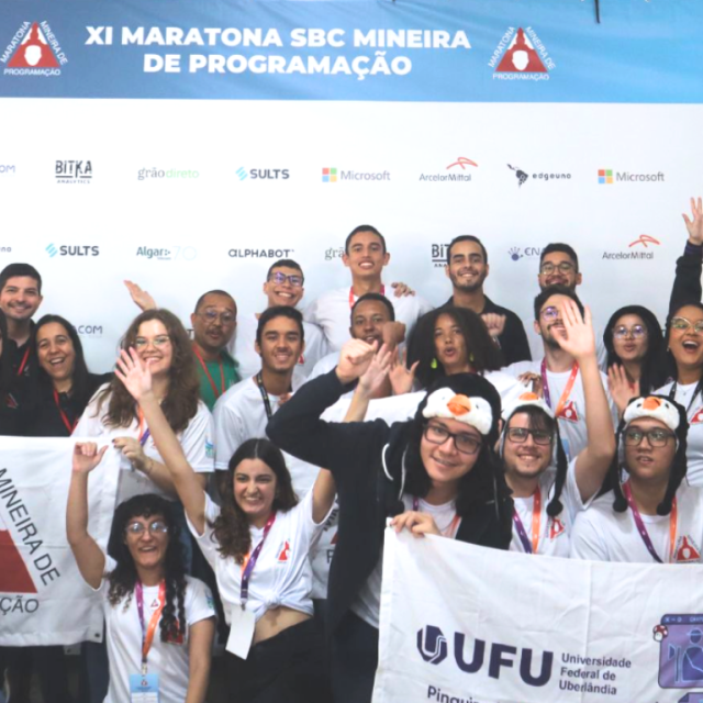 Foto dos estudantes de Computação da UFU, em frente ao banner da Maratona Mineira de Programação