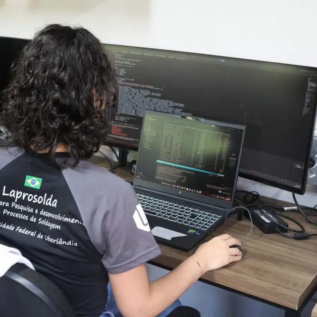 Uma mulher mexendo no computador, dentro do laboratório do Lapsolda, com a tela cheia de códigos de software